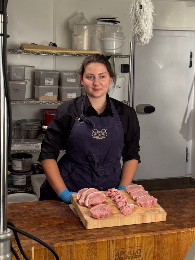 Young female butcher stood behind wooden chopping board with cuts of pork meat on it